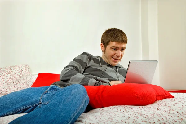 Jovem homem casual trabalhando com computador na cama — Fotografia de Stock