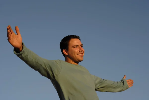 Young man with arms wide open at sunset light — Stock Photo, Image