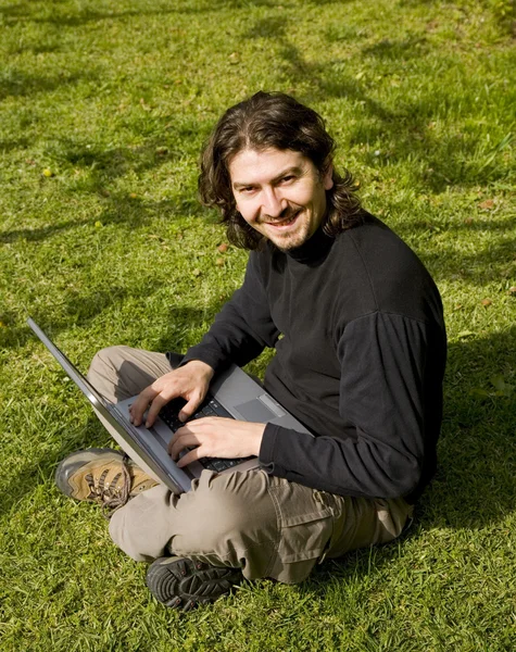 Jovem trabalhando com laptop na grama — Fotografia de Stock