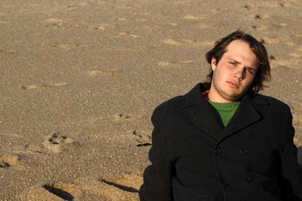 Plajda kuma oturan genç adam — Stok fotoğraf