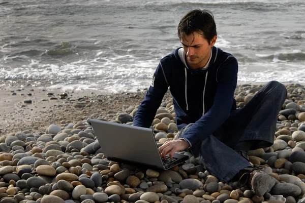 Ung, tilfeldig mann med bærbar PC på stranden – stockfoto