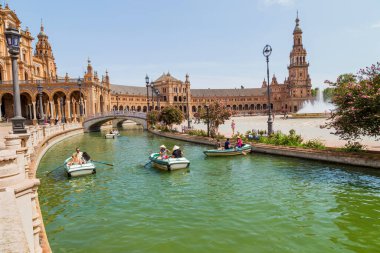 Seville, Endülüs, İspanya: Plaza de Espana Meydanı 'ndaki merkez Rönesans binası, Guadalquivir nehrinin gündüz tekneleri ve insanlarla manzarası.