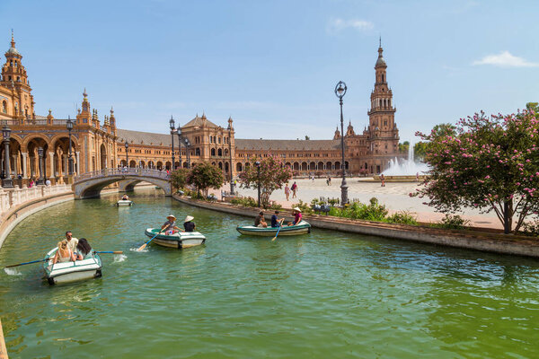 Seville, Andalusia, Spain: Central Renaissance building in Plaza de Espana square, view of Guadalquivir river with boats and people in the day time.