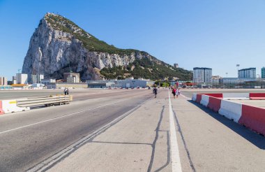 Cebelitarık, İngiltere. Arka planda Cebelitarık Kayası 'nın olduğu Cebelitarık Havalimanı' ndaki pistten geçen yerel halk ve arabalar. Cebelitarık, İngiliz Denizaşırı Toprakları, İngiltere.