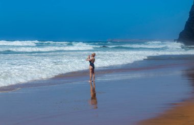 Sagres, Portekiz: Dalgaların arasında plajda yoga yapan rahat bir kadın. Sagres, Algarve. Portekiz