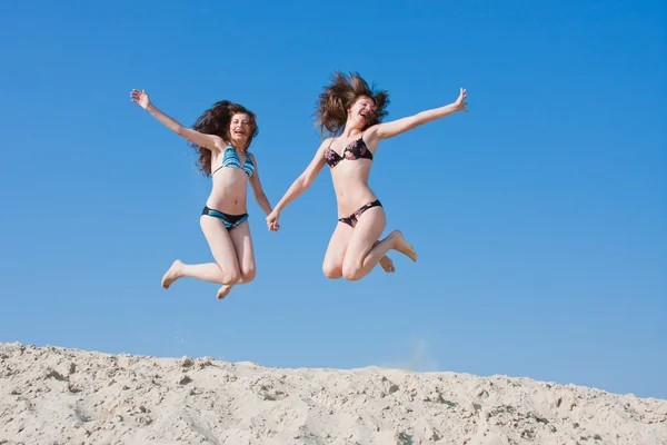 Twee vrouwen in Zwemmen kostuums springen op zand — Stockfoto