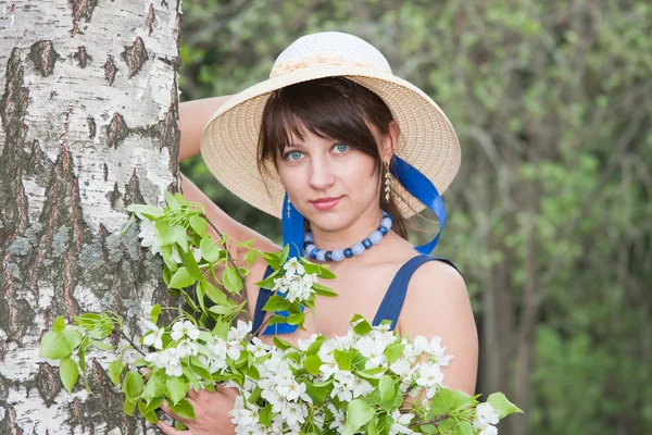 Mujer en un sombrero cerca de un abedul con ramitas de manzana floreciente-t —  Fotos de Stock