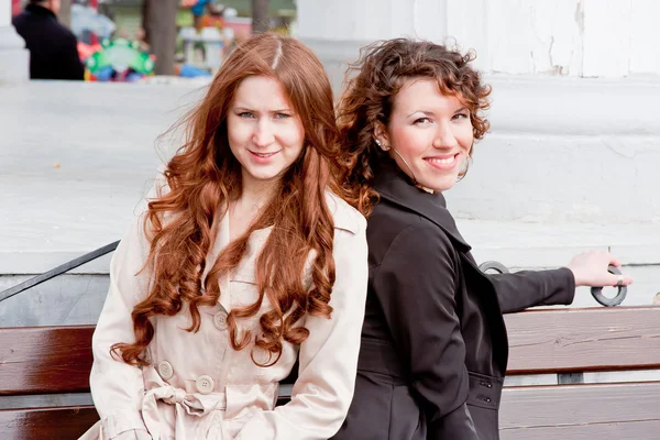 Two beautiful women in a park sit on a bench — Stock Photo, Image