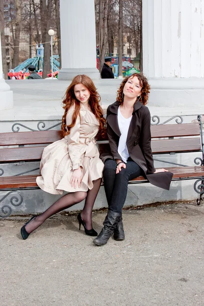 Two beautiful women in a park sit on a bench — Stock Photo, Image