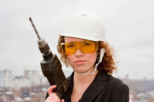 Mulher de negócios em um capacete e óculos com uma broca na mão — Fotografia de Stock