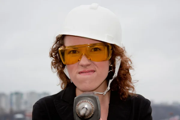 Γυναίκα των επιχειρήσεων σε ένα κράνος και γυαλιά με ένα τρυπάνι στο χέρι — Φωτογραφία Αρχείου