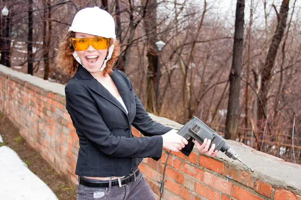 Mulher de negócios em um capacete e óculos com uma broca na mão — Fotografia de Stock