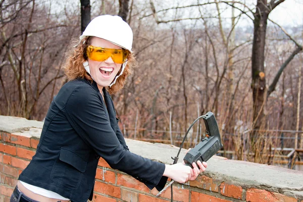 Mulher de negócios em um capacete e óculos com uma broca na mão — Fotografia de Stock