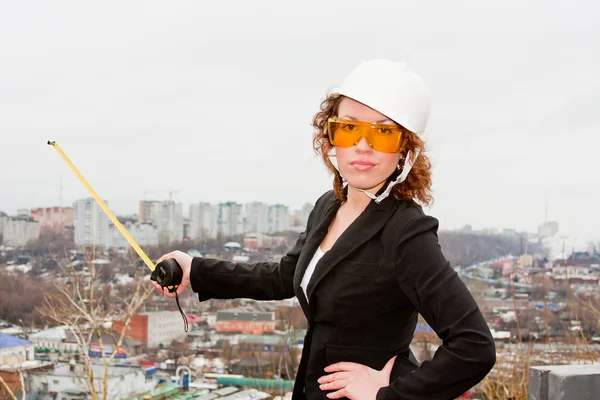 Business woman in a helmet and goggles with tape measure in han — Stock Photo, Image