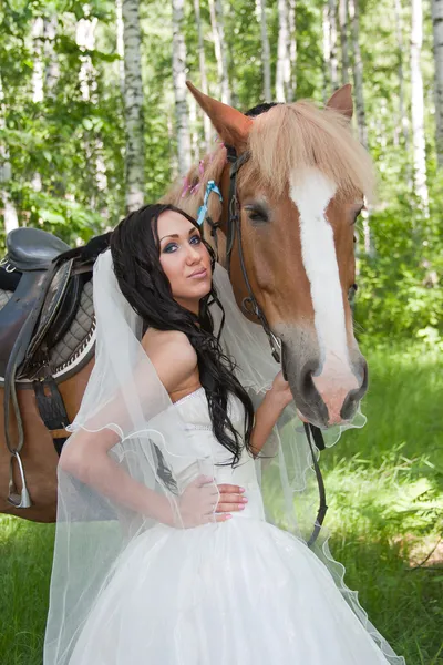 Jovem no vestido de noiva ao lado de um cavalo — Fotografia de Stock