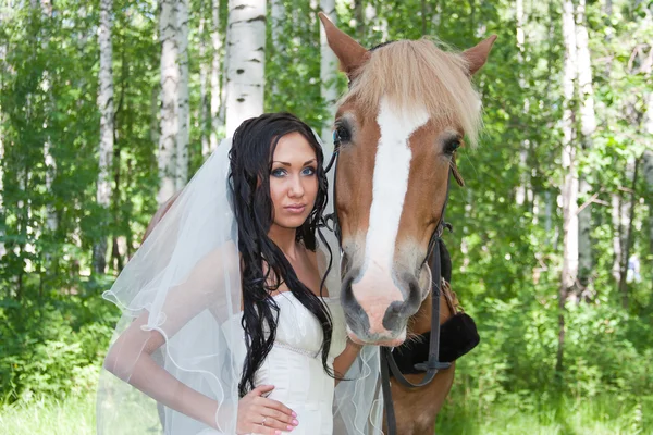 Jovem no vestido de noiva ao lado de um cavalo — Fotografia de Stock