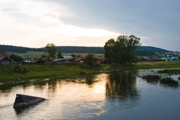 Obec je na břehu řeky při západu slunce — Stock fotografie