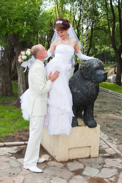 Happy groom and fiancee in a park near the sculpture of dog — Stock Photo, Image