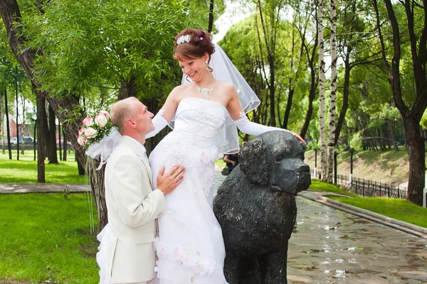 Happy groom and fiancee in a park near the sculpture of dog — Stock Photo, Image