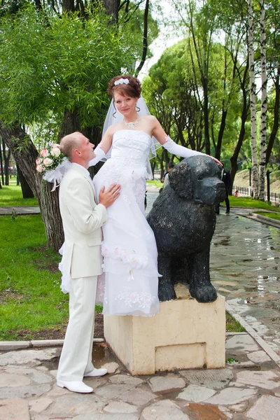 Noivo feliz e noiva em um parque perto da escultura do cão — Fotografia de Stock