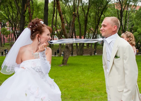 Fiancee holds teeth a tie for a groom in a park on nature