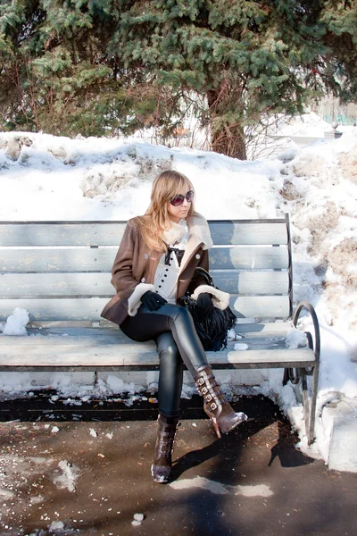 Žena ve winter parku sedí na lavičce — Stock fotografie