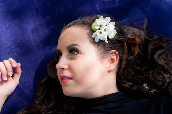 Une jeune femme avec une fleur dans les cheveux repose sur un fond bleu — Photo