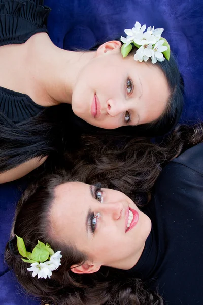 two young women with flowers in hair lie on a blue background