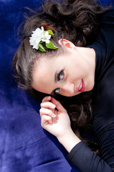 A young woman with a flower in hair lies on a blue background — Stock Photo, Image