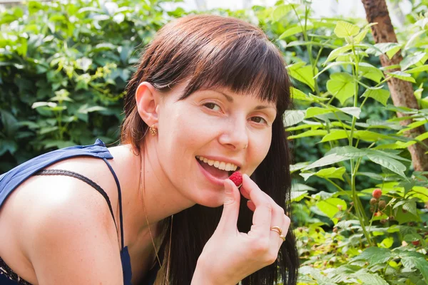 En ung kvinna äter bär hallon i en trädgård — Stockfoto