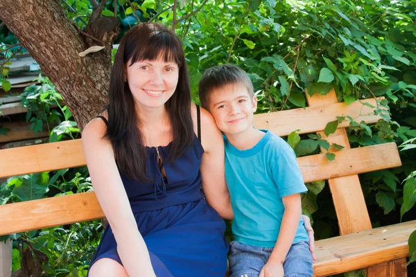 Moeder met een zoon zitten op een bankje in een tuin — Stockfoto