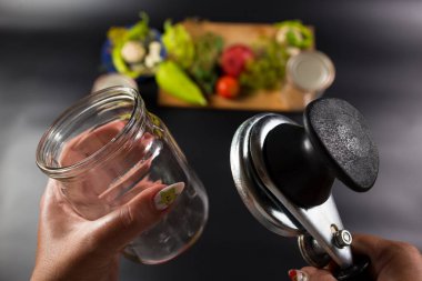 Kadın elleri cam şişeli konserve anahtarını tutuyor ve arka planda taze sebzeler var..