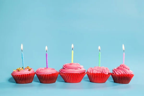 Birthday cupcakes with candles, on blue background with copy space.