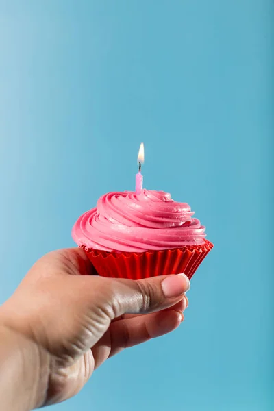女性の手を保持カップケーキとともに誕生日キャンドルを閉じます 青の背景に — ストック写真