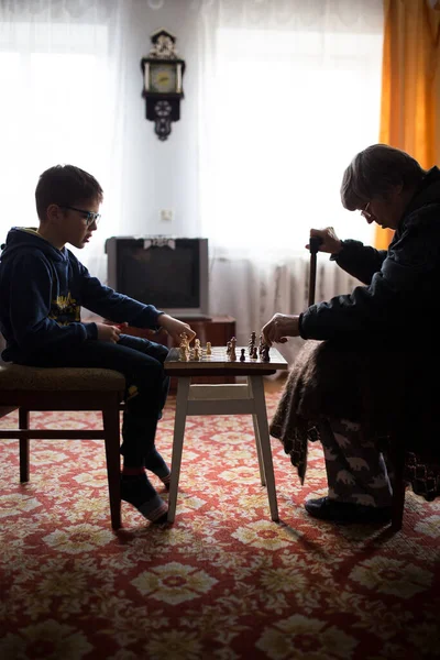 小さな男の子遊びチェスで老婦人でライフスタイル部屋とともに自然光から窓 — ストック写真