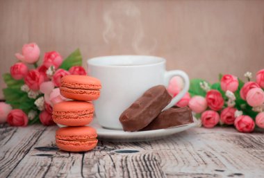 Üç portakallı kurabiye bir kulede dizilmiş bir fincan çay ve çikolata ile şakayık çiçeklerinin arka planında