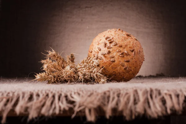 Rolo de pão e trigo orelhas ainda vida — Fotografia de Stock