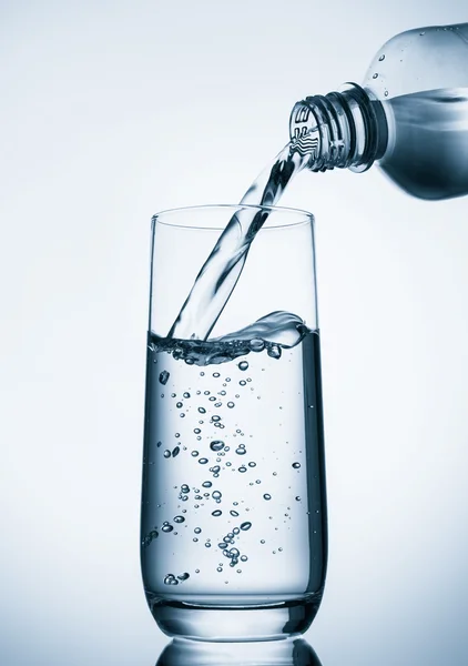 Menuangkan air ke kaca dari botol dengan latar belakang biru — Stok Foto