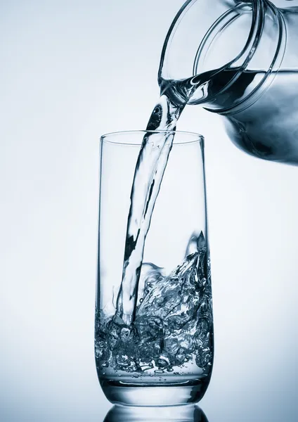 Gießen von Wasser aus Glaskannen auf blauem Hintergrund — Stockfoto