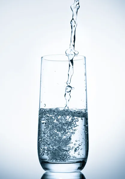 Wasser gießt in Glas auf blauem Hintergrund — Stockfoto