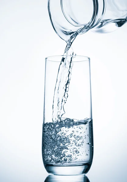 Gießen von Wasser aus Glaskannen auf blauem Hintergrund — Stockfoto