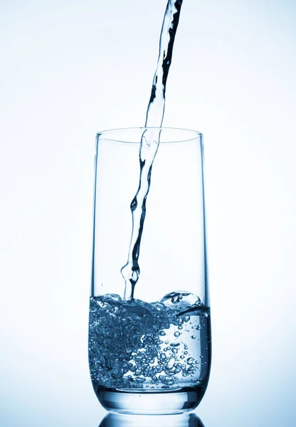 青色の背景にガラスに注ぐ水 — ストック写真