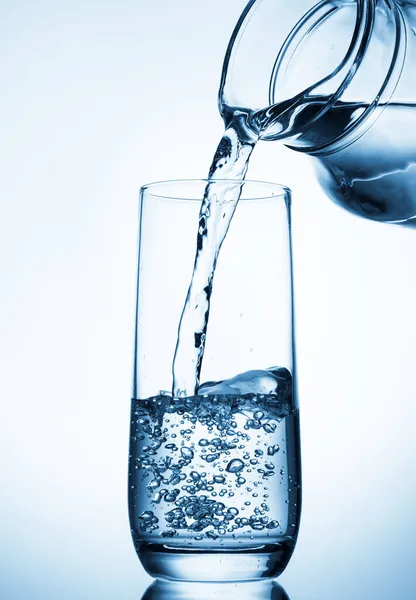 stock image Pouring water from glass pitcher on blue background..