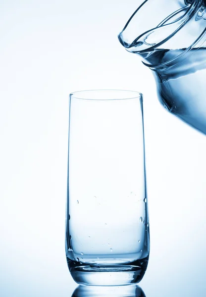 Gießen Von Wasser Aus Glaskannen Auf Blauem Hintergrund — Stockfoto