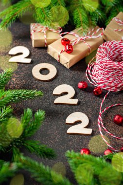 - Mutlu yıllar. Kırmızı Noel süsleri ve Noel ağacının yanında paketlenmiş hediyeler. Ahşap numaraları 2022 olan şenlikli bir arka plan.