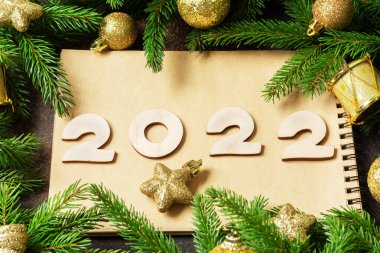 - Mutlu yıllar. Noel ağacının dallarında sarı ya da altın Noel süslemeleri. Ahşap numaraları 2022 olan şenlikli bir arka plan.