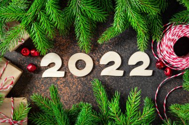 - Mutlu yıllar. Kırmızı Noel süsleri ve Noel ağacının yanında paketlenmiş hediyeler. Ahşap numaraları 2022 olan şenlikli bir arka plan. Üst görünüm