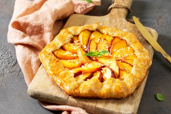 French galette or peach pie on a wooden serving board on a dark culinary background closeup. Summer homemade sweet pastries