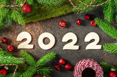 - Mutlu yıllar. Kırmızı Noel süsleri ve Noel ağacının yanında paketlenmiş hediyeler. Ahşap numaraları 2022 olan şenlikli bir arka plan. Üst görünüm