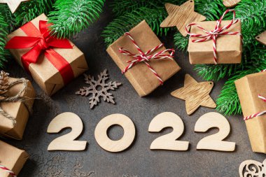 Noel ya da Yeni Yıl bayrağı, köknar dalları, kırmızı ve beyaz kurdele ve çevre dostu el sanatları paketlerinde hediye kutuları. Ahşap numaraları 2022 olan şenlikli bir arka plan. Üst görünüm